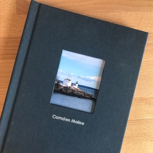 Custom Photo Book Design-Photo book with navy linen cover, photo of lighthouse and Camden Maine text on wood table